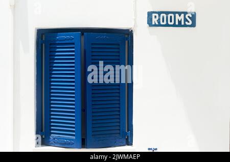 Window with blue shutters on white wall with Rooms sign Stock Photo