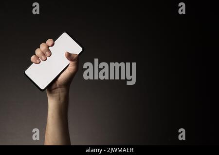 Man's hand holding smart phone with blank white screen isolated on dark background with copy space Stock Photo