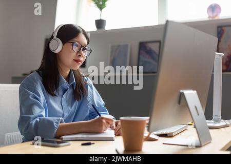 Asian Businesswoman Working On Computer And Taking Notes In Office Stock Photo
