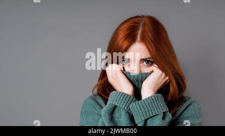 shy or embarrassed woman pulling turtleneck sweater over face Stock Photo