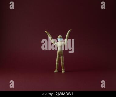 Wooden mannequin with protective surgical mask in purple backgound Stock Photo