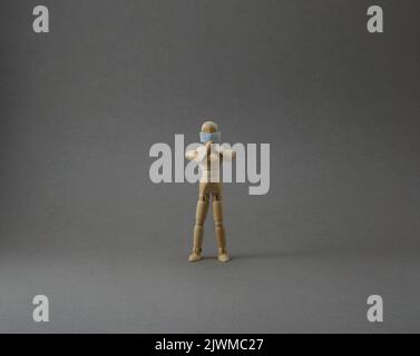 Wooden mannequin with protective surgical mask in grey backgound Stock Photo