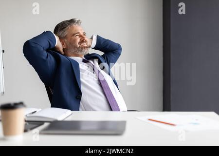 Smiling middle aged businessman leaning back in chair at workplace in office Stock Photo