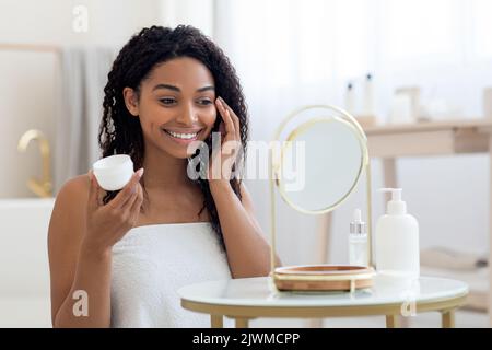 Attractive Young African American Woman Applying Moisturising Cream On Face Stock Photo