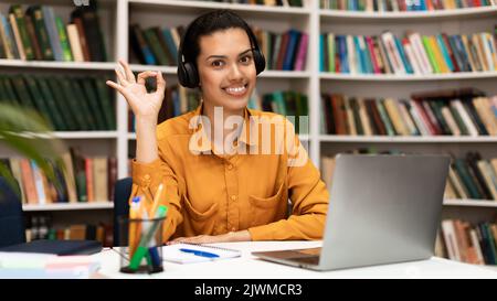 E-learning concept. Happy young female teacher giving online lesson on laptop, showing OK gesture and smiling Stock Photo