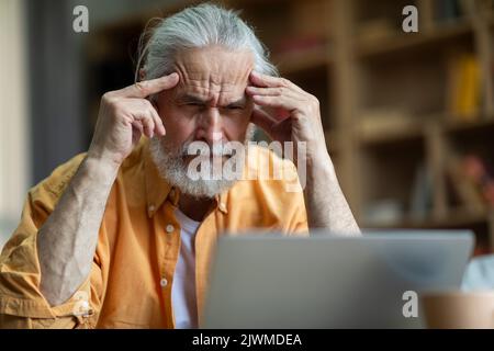 Stressed senior man working from home, using laptop Stock Photo