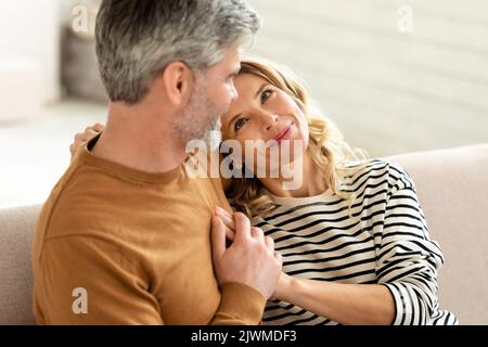 Cheerful Middle Aged Couple Embracing Sitting On Couch At Home Stock Photo