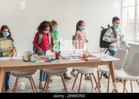 Diverse School Kids With Backpacks Wearing Face Masks Entering Classroom Stock Photo