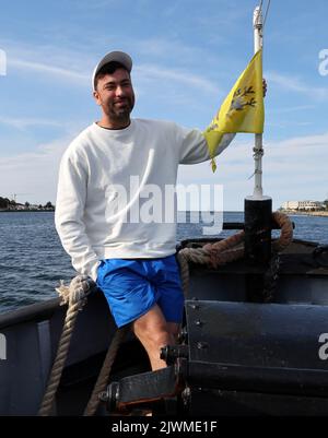 06 September 2022, Mecklenburg-Western Pomerania, Warnemünde: Rapper Marteria drives with a historic tugboat to the Warnemünde pier, where he wants to give away about 500 fish rolls to his fans. With the action Marteria wants to make advertising for his stadium concert on 02.09.2023 in Rostock, because in addition to the rolls there were also codes for an advance sale of tickets. Photo: Bernd Wüstneck/dpa Stock Photo