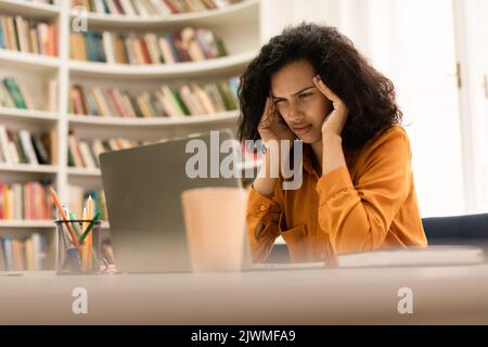 Lack of inspiration. Thoughtful female student looking on laptop screen, sitting in modern library Stock Photo