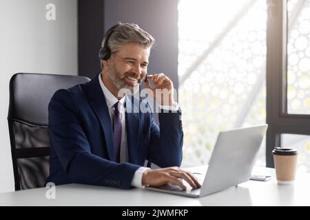 Middle aged businessman with headset and laptop making video conference with partners Stock Photo