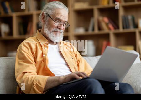 Old man in eyeglassses using modern laptop at home Stock Photo