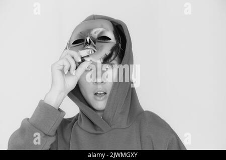 The girl removes a plastic mask from her face and is surprised on an isolated background, black and white photo, remove the mask from her face Stock Photo