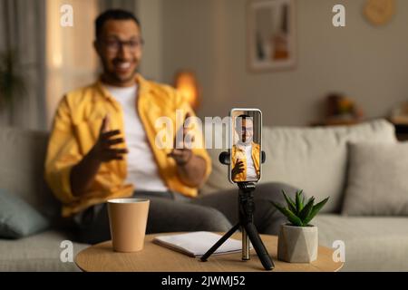 Happy young black teacher giving online lecture, using smartphone to communicate with students from home Stock Photo