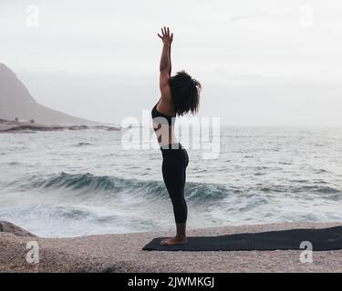 Beautiful young woman sitting in lotus pose with Raised Arms at the beach  with sea background.