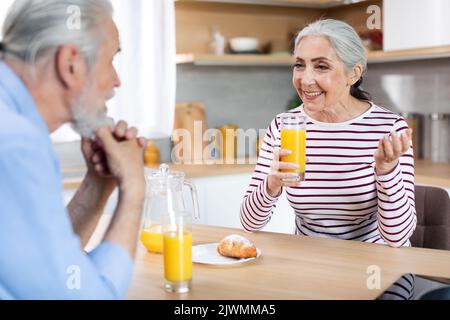 Happy Senior Spouses Chatting While Having Breakfast In Kitchen Together Stock Photo