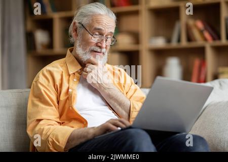 Cheerful senior man using laptop at home Stock Photo