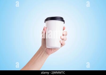 Male hand holding a white coffee cup isolated on light blue background. Stock Photo