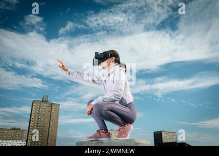 Woman outside wearing virtual reality headset with her arm outstretched, urban backdrop. Stock Photo