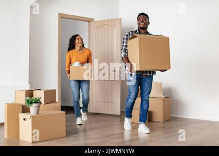 Excited African Couple Carrying Moving Boxes Looking At New House Stock Photo