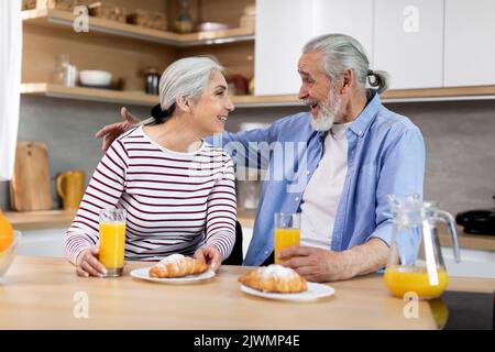 Portrait Of Happy Senior Spouses Having Snacks In Kitchen Together Stock Photo