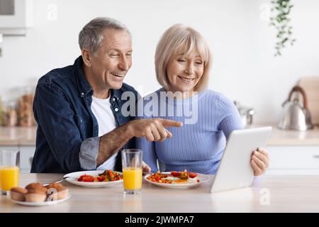 Cheerful elderly couple using digital tablet while having breakfast Stock Photo