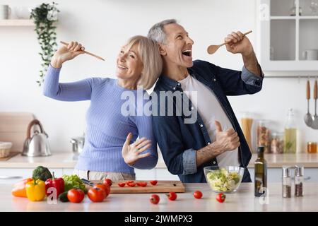 Senior husband and wife having fun while cooking, singing songs Stock Photo