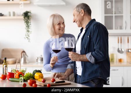 Positive elderly spouses drinking red wine while preparing meal Stock Photo