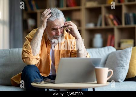 Upset elderly man using laptop, having phone conversation Stock Photo