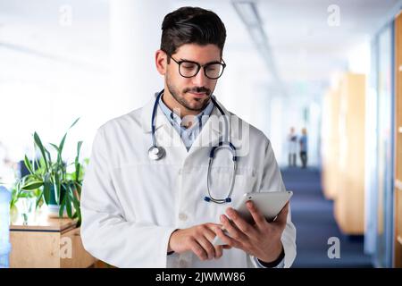 Portrait of male doctor standing in a medical clinic. Doctor in lab coat holding a digital tablet and working. Stock Photo