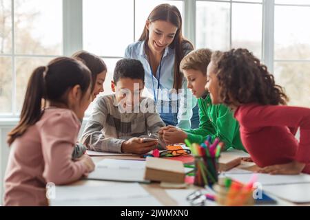 Multiethnic School Kids And Teacher Using Smartphone In Modern Classroom Stock Photo
