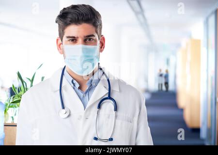 Portrait of male doctor. Healthcare professional is wearing protective face mask. He is in hospital during coronavirus crisis. Stock Photo