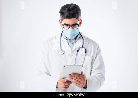 Studio shot of maled doctor wearing face mask and using digital tablet while standing at isolated background. Copy space. Stock Photo