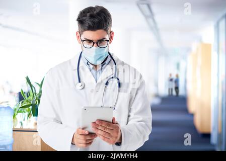 Portrait of mature male doctor using touchpad and working in clinic. Healthcare professional is wearing protective face mask. He is in hospital during Stock Photo