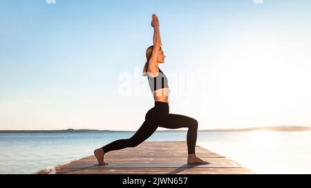 Sporty Middle Aged Female Doing Yoga Outdoors, Standing In Warrior 1 Pose Stock Photo