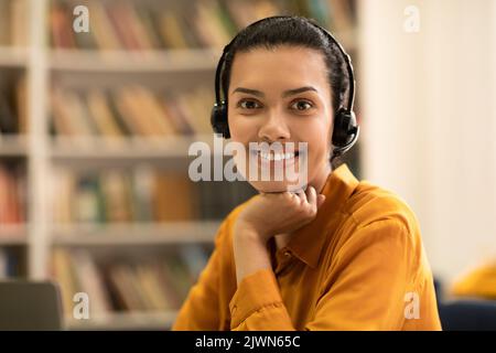 E-teaching concept. Portrait of happy woman in headset sitting in library and smiling at camera Stock Photo