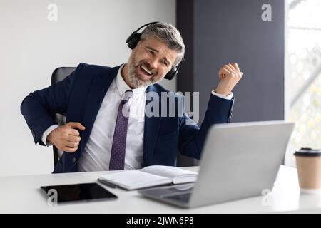 Positive Middle Aged Businessman Listening Music In Headphones And Playing Virtual Guitar Stock Photo