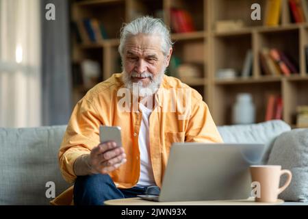 Happy senior businessman working from home, using laptop and phone Stock Photo