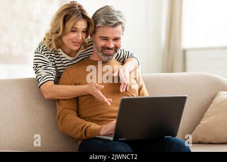 Wife Hugging Husband While He Working Online On Laptop Indoor Stock Photo