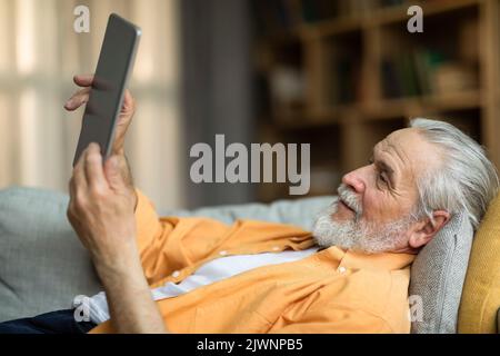Positive senior man using digital tablet at home, side view Stock Photo
