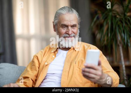 Cheerful old man using mobile phone at home Stock Photo