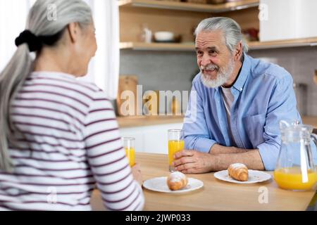 Senior Married Couple Chatting While Having Breakfast Together In Kitchen Stock Photo