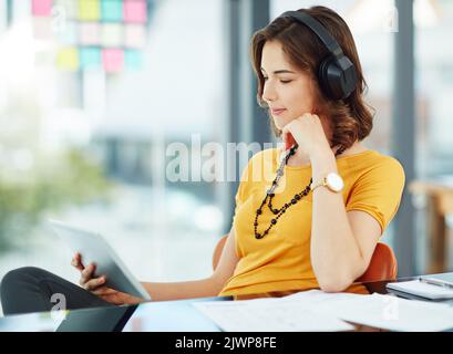 Watching a show in her free time. a young businesswoman watching something on her tablet while sitting in the office. Stock Photo