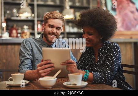 Sharing what they love. a young couple using a digital tablet together on a coffee date. Stock Photo