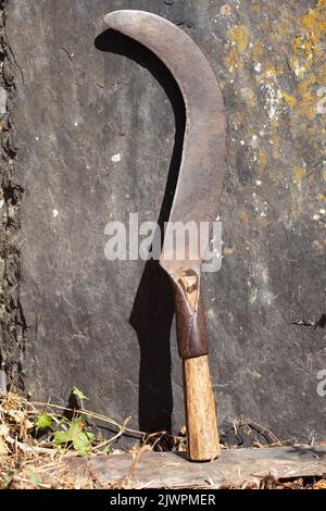 an old hand-forged sickle sits on a large black slate. Stock Photo