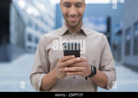 Close up photo selective focus african american man typing message on phone smiling and happy businessman using smartphone. Stock Photo