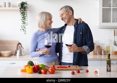Cheerful senior man and woman cooking together, drinking wine Stock Photo