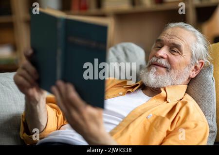 Relaxed grandfather chilling on couch, reading book Stock Photo