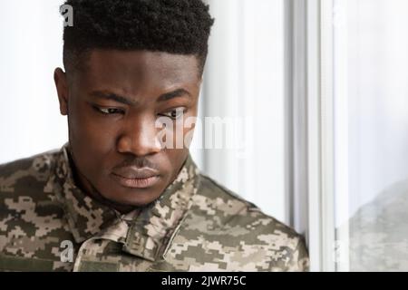 Unhappy military black man standing next to window Stock Photo