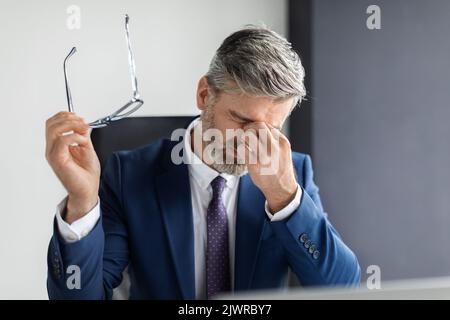 Portrait Of Tired Middle Aged Businessman Suffering Eye Strain At Workplace Stock Photo